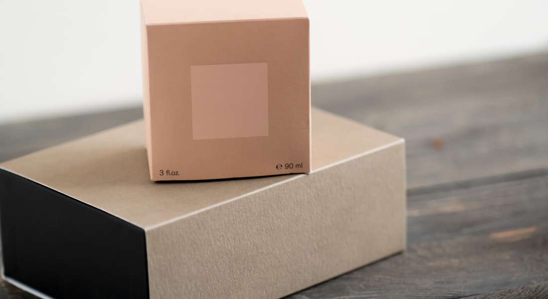 Two minimally designed cardboard packages sit on a wooden surface. The background behind the boxes is white.