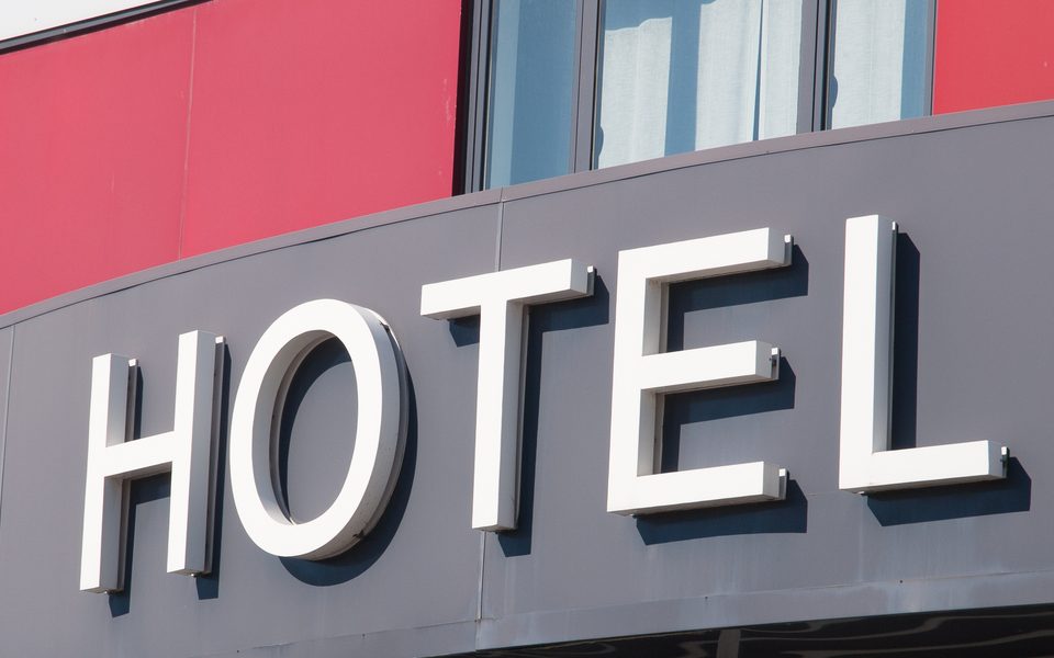 The façade of a hotel building has several windows lining the front between red walls, and a large sign reads "HOTEL."