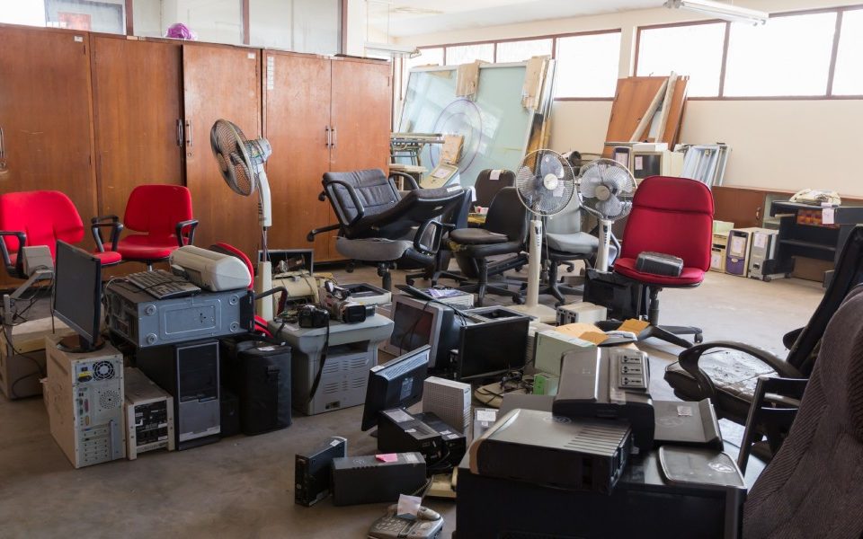 A selection of abandoned office equipment, including chairs, computers, and printers, sit in the center of a room.