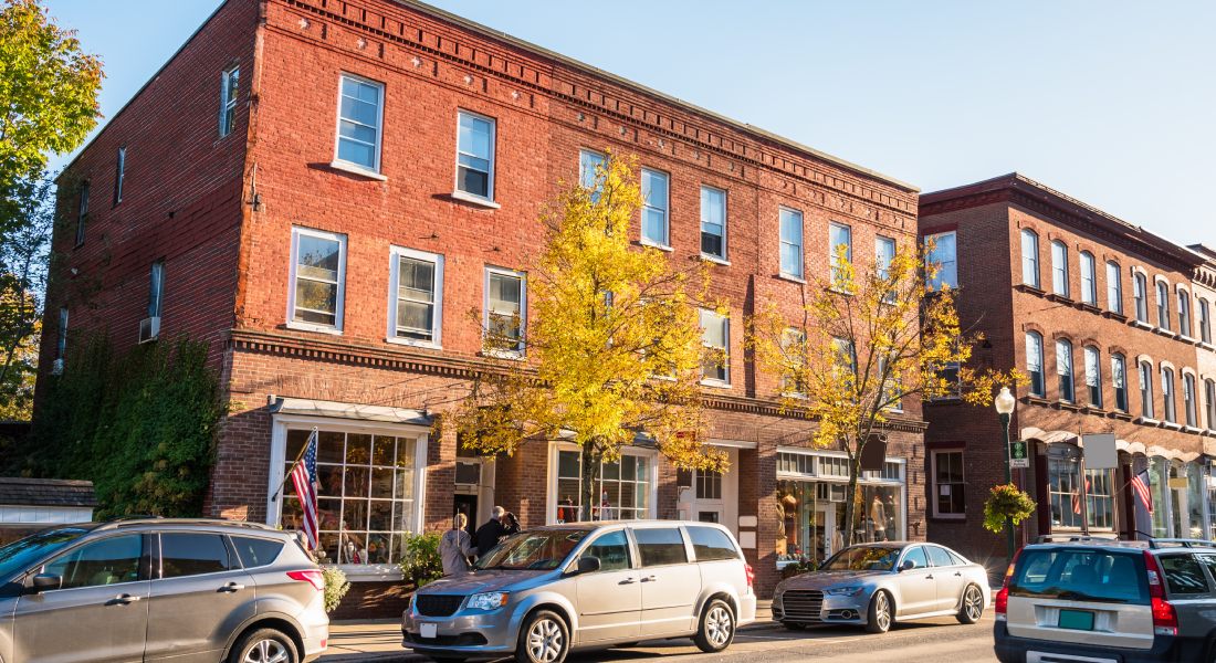 The exterior of a multi-level brick building with storefronts on the street level. There are cars parked along the street.