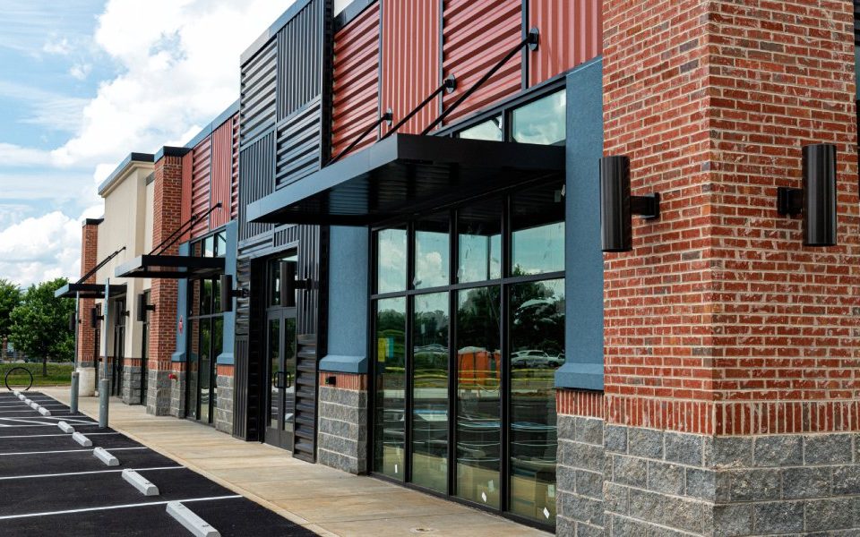 A business building contains a black metal, red brick, and tan stone exterior. The parking spaces are empty.