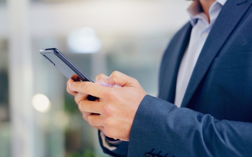 A person in a clean blue suit is standing outside and using their thumbs to text on their cell phone.