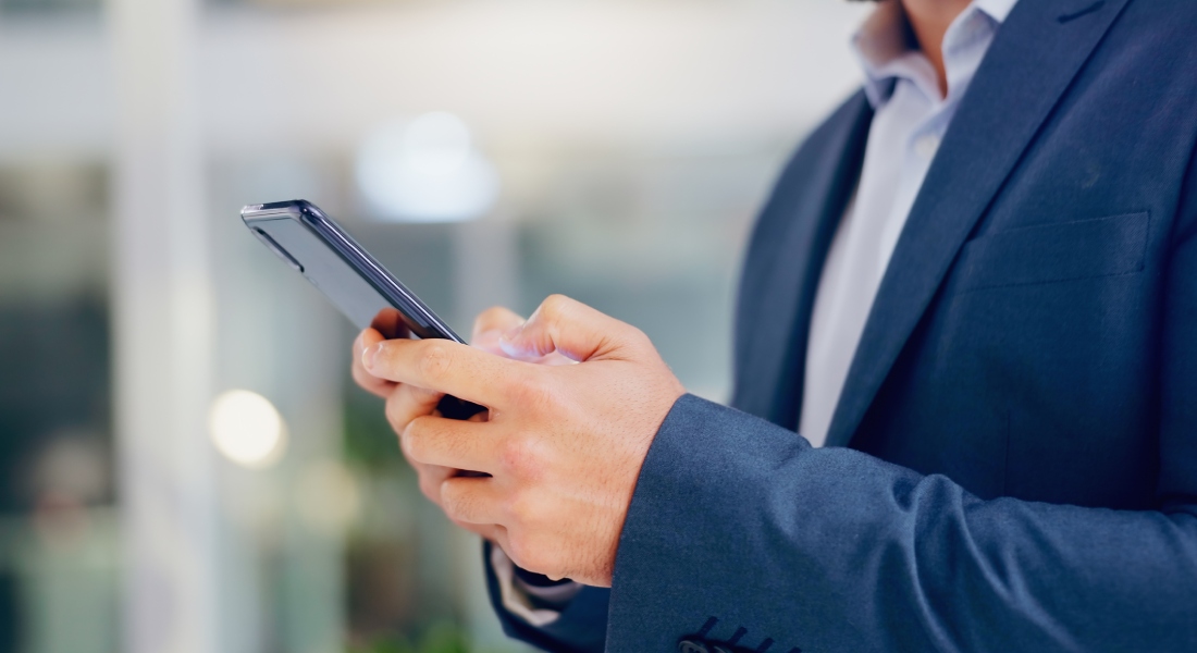 A person in a clean blue suit is standing outside and using their thumbs to text on their cell phone.