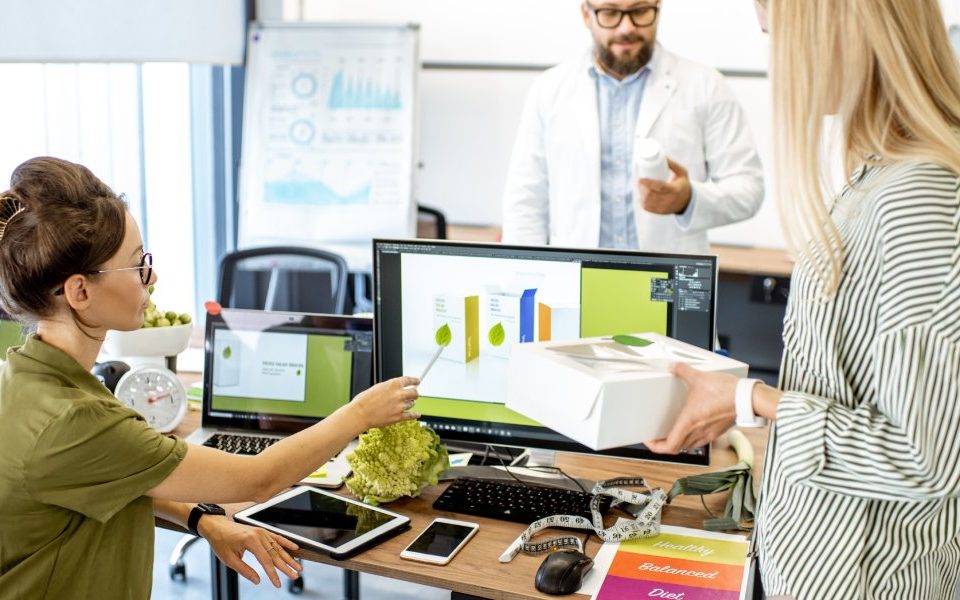 Three brand strategists working together on packaging design. One is at the computer and the other two are standing up.