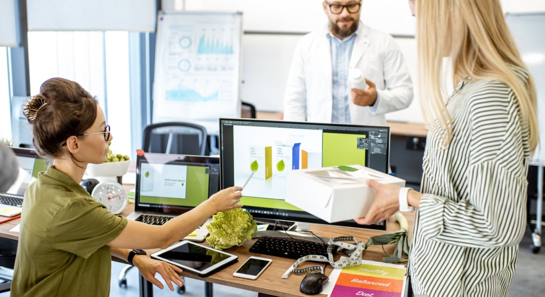 Three brand strategists working together on packaging design. One is at the computer and the other two are standing up.