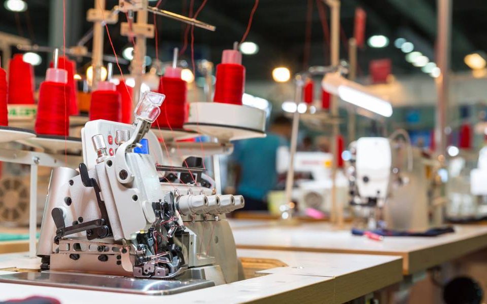 An overlock sewing machine with multiple cones of red thread and a straight sewing machine sit inside a warehouse.