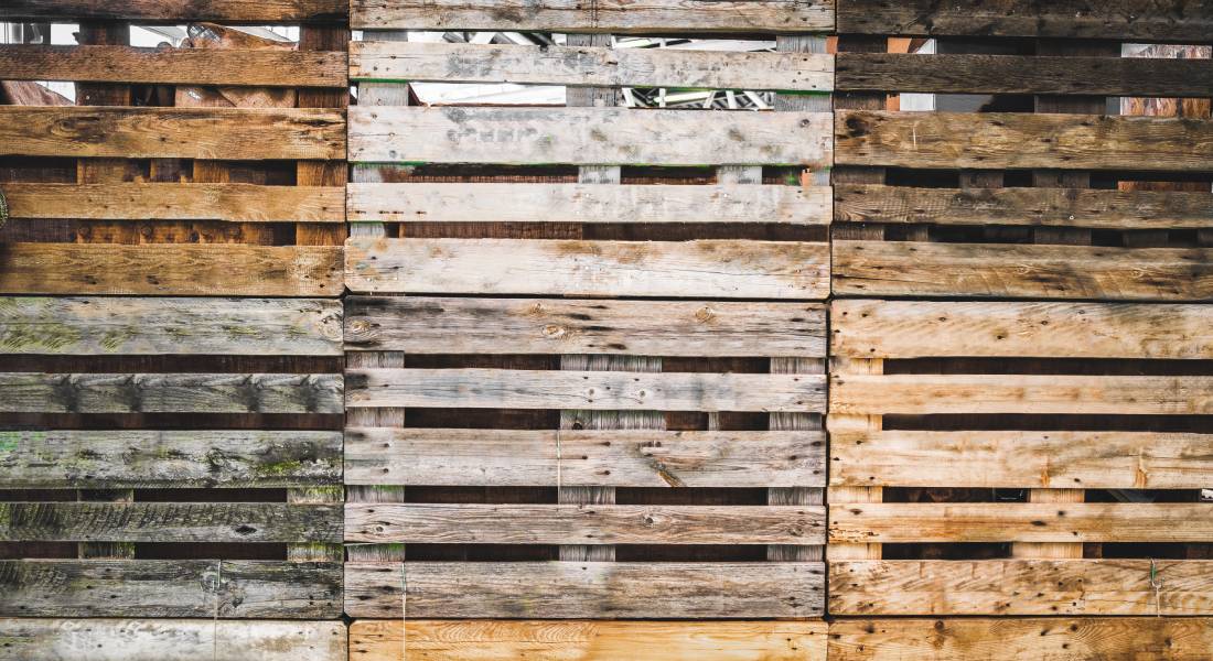 Wooden pallets of different textures and shades are stacked one on top of another. Each pallet has 5 slats.